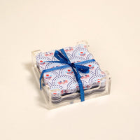 The Darling Effect’s All-American Darling Table Talk Acrylic Coaster Set features a patriotic red, white, and blue design, stacked in a clear holder with a blue ribbon—perfect for festive table décor on any occasion.