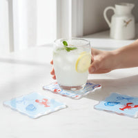 A hand holds a glass of iced drink with lemon and mint on a Harbor House Table Talk Acrylic Coaster by The Darling Effect, adorned with lobsters and shells. Two matching coasters complete the charming table décor.