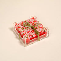 The Darling Effect’s Strawberry Fields Table Talk Acrylic Coaster Set features floral coasters in a clear acrylic holder, tied with a green ribbon—adding charming table décor to any plain light background.