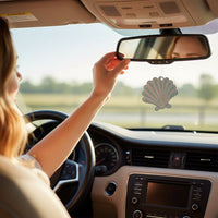 A woman drives, adjusting The Darling Effect’s Seashell Sweet Ride Car Air Freshener on her mirror. Sunlight streams in, filling the car with a unique, long-lasting aroma as the scenery blurs past.