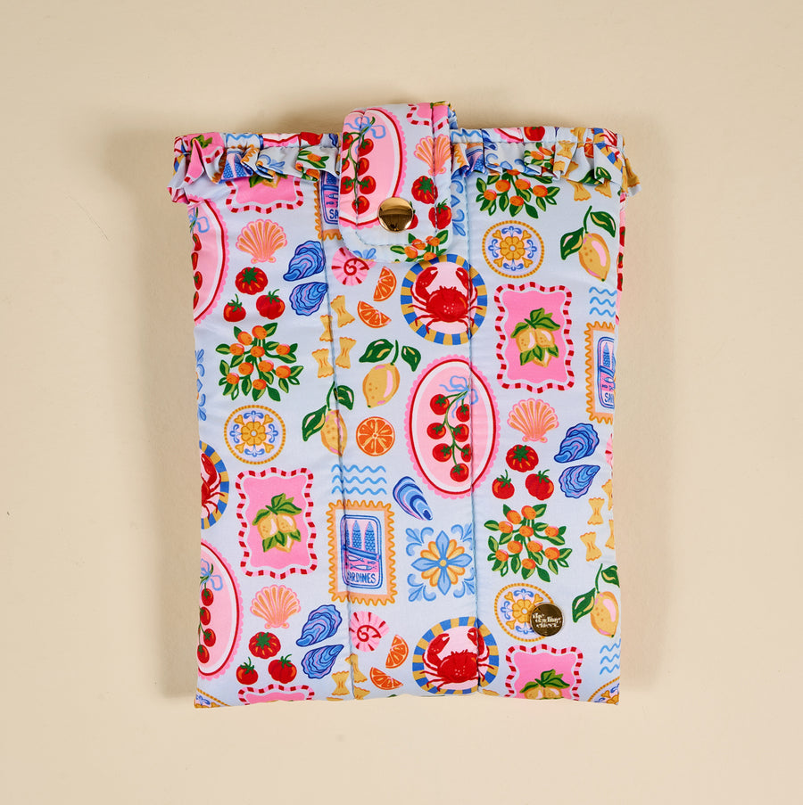 The Darling Effect's Ciao Bella Book Cover features a light beige background with playful fruit and plate motifs, a ruffled top, and button closure—offering charming protection for your books.