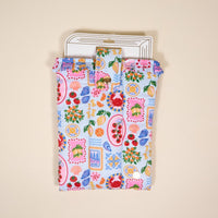 The Darling Effect's Ciao Bella Book Cover is a colorful, cute pouch with a flap featuring fruit, plate, and kitchen item patterns, shown lying flat on a neutral background with a white card partially inside.