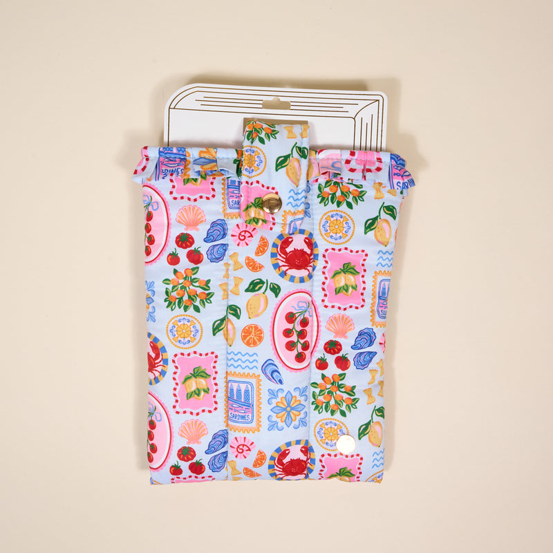 The Darling Effect's Ciao Bella Book Cover is a colorful, cute pouch with a flap featuring fruit, plate, and kitchen item patterns, shown lying flat on a neutral background with a white card partially inside.