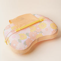 The Darling Effect Daisy Craze Peach Ballast Beach Pillow is a limited-edition pastel floral pillow in yellow, orange, and pink, featuring a yellow strap and attached peach pouch, shown on a light beige background.
