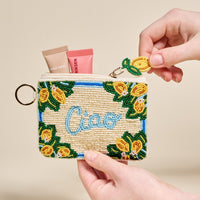 The Darling Effect's Ciao Handcrafted Beaded Pouch, featuring a lemon and "Ciao" design, is shown held in hands with two small makeup tubes inside.