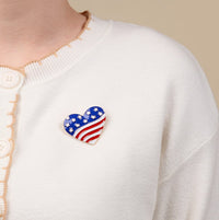 The Darling Effect’s Americana Heart Timeless Brooch, elegantly styled, is worn on a cream-colored cardigan.