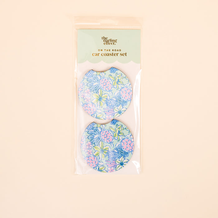 A set of two absorbent car coasters from the-darling-effect, featuring a pastel floral pattern in blue, pink, and green. Coastal Cove On the Road Car Coaster Set is displayed against a light beige background.