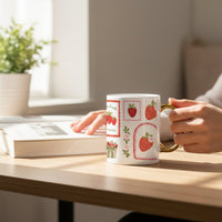 A person enjoys coffee and tea from The Darling Effect’s Strawberry 11 oz Cozy Cute Ceramic Mug while reading a book at a wooden table. Sunlight shines in, and a potted plant is visible in the background.