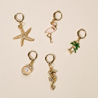 The Darling Effect’s Paradise Cove The Ultimate Charm Pack features gold earrings with starfish, flamingo, palm tree, pearl seashell, and seahorse charms—ideal for pairing with bold necklaces or mixing into your favorite set.