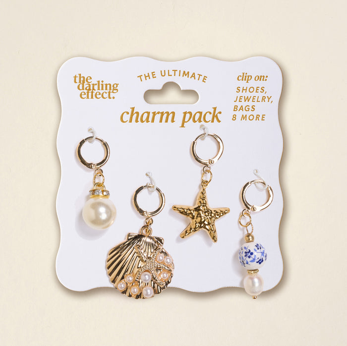 The Darling Effect’s Under the Sea The Ultimate Charm Pack includes four gold clip-on charms—a pearl, a pearl-accented seashell, a textured starfish, and a blue-and-white bead with pearl—ideal for scrunchie charm sets.