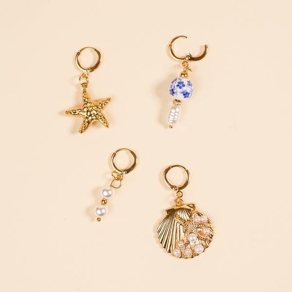 Four gold hoops from The Darling Effect’s Under the Sea The Ultimate Charm Pack are shown on beige: one with a starfish, one with a blue-and-white bead and pearl, one with three pearls, and one seashell charm adorned with pearls.
