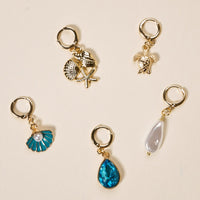 Ocean Treasures The Ultimate Charm Pack by The Darling Effect: five unique gold keyrings—shell & starfish, angel, blue seashell, blue teardrop gem & white pearl—on beige. Perfect for statement necklaces or pairing with a scrunchie charm set.