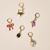 The Darling Effect’s Party in the USA The Ultimate Charm Pack features five gold keychains—a star, American flag, red bow, blue gem, and clear gem with gold rings—ideal for scrunchie charm sets or pairing with statement necklaces.