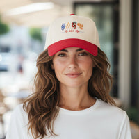 A woman smiles, wearing The Darling Effect’s La Dolce Vita Classic Canvas Hat—a cream cap with a red brim, colorful embroidered fruit, and the phrase "la dolce vita," perfect for laid-back, everyday style.