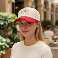 A young woman wears The Darling Effect's La Dolce Vita Classic Canvas Hat in cream and red, featuring embroidered fruits and "la dolce vita"—perfect for a relaxed, stylish look.