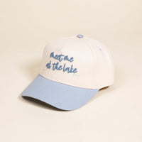The Darling Effect’s Meet Me at the Lake Classic Canvas Hat features a cream canvas, light blue brim and top button, and blue “meet me at the lake” embroidery with wavy lines for effortless casual style.