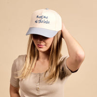 A woman models The Darling Effect's Meet Me at the Lake Classic Canvas Hat in beige and light blue, paired with a relaxed fit beige top, exuding effortless casual style against a matching background.