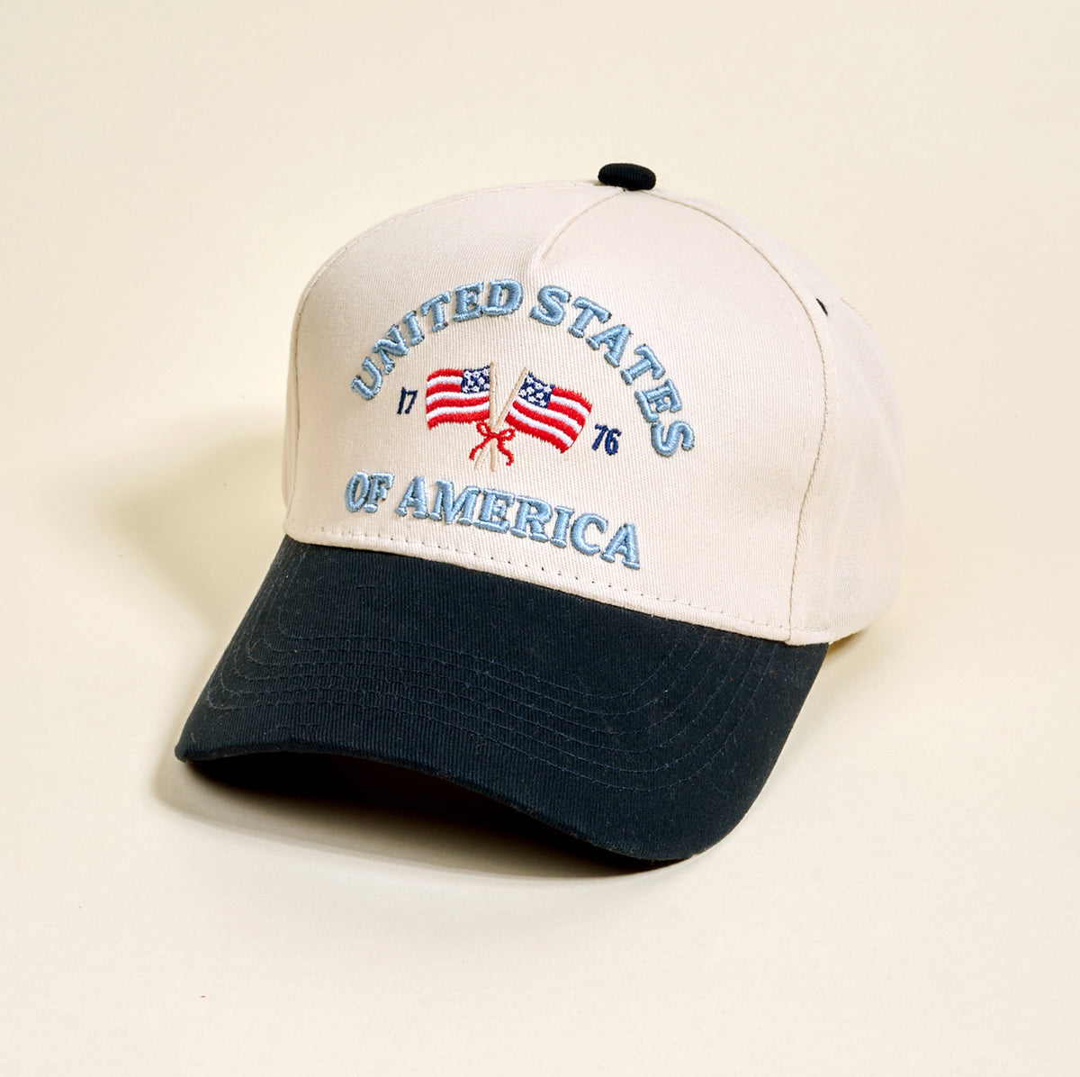 The Darling Effect's United States of America Classic Canvas Hat features beige and black colors, "UNITED STATES OF AMERICA" and "1776" embroidery, plus two crossed flags—ideal for a comfortable, laid-back style.