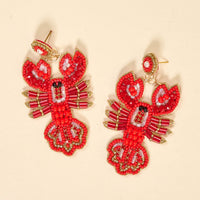 The Darling Effect’s Lobster Beaded Earrings feature a vibrant, hand-beaded red lobster design with gold accents, displayed on a light beige background—an eye-catching accessory that brings a playful flair to your jewelry collection.