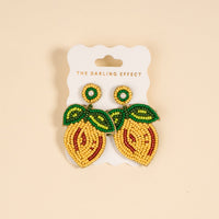 The Darling Effect’s Lemon Beaded Earrings feature vibrant, lemon shapes with green leaf details and white pearl accents, displayed on a card labeled with the brand name.