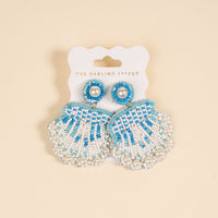Seashell Beaded Earrings by The Darling Effect feature playful blue and white beaded shells with pearl accents, displayed on a white card labeled with the brand name.