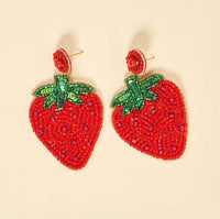 The Darling Effect’s Strawberry Beaded Earrings feature bright red beads with green sequin leaves and small red accents, displayed against a light background.