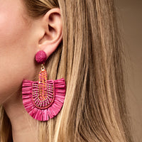 Close-up of a woman's ear wearing The Darling Effect's Hot Pink Fringe Earrings—large, lightweight statement earrings with woven and beaded details. Perfect boho style for everyday wear; long straight blonde hair is partially visible.
