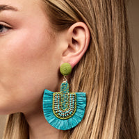A close-up of a woman wearing The Darling Effect’s Teal Fringe Earrings—lightweight boho style with a green stud, blue beaded arch, and bright blue fringes. Her loose blonde hair adds to the effortless, everyday look.