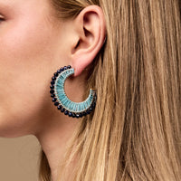 Close-up of a woman's ear wearing The Darling Effect's Coastal Blue It-Girl Earrings—crescent-shaped hoops with turquoise raffia and navy blue beads, perfect lightweight earrings for everyday wear.