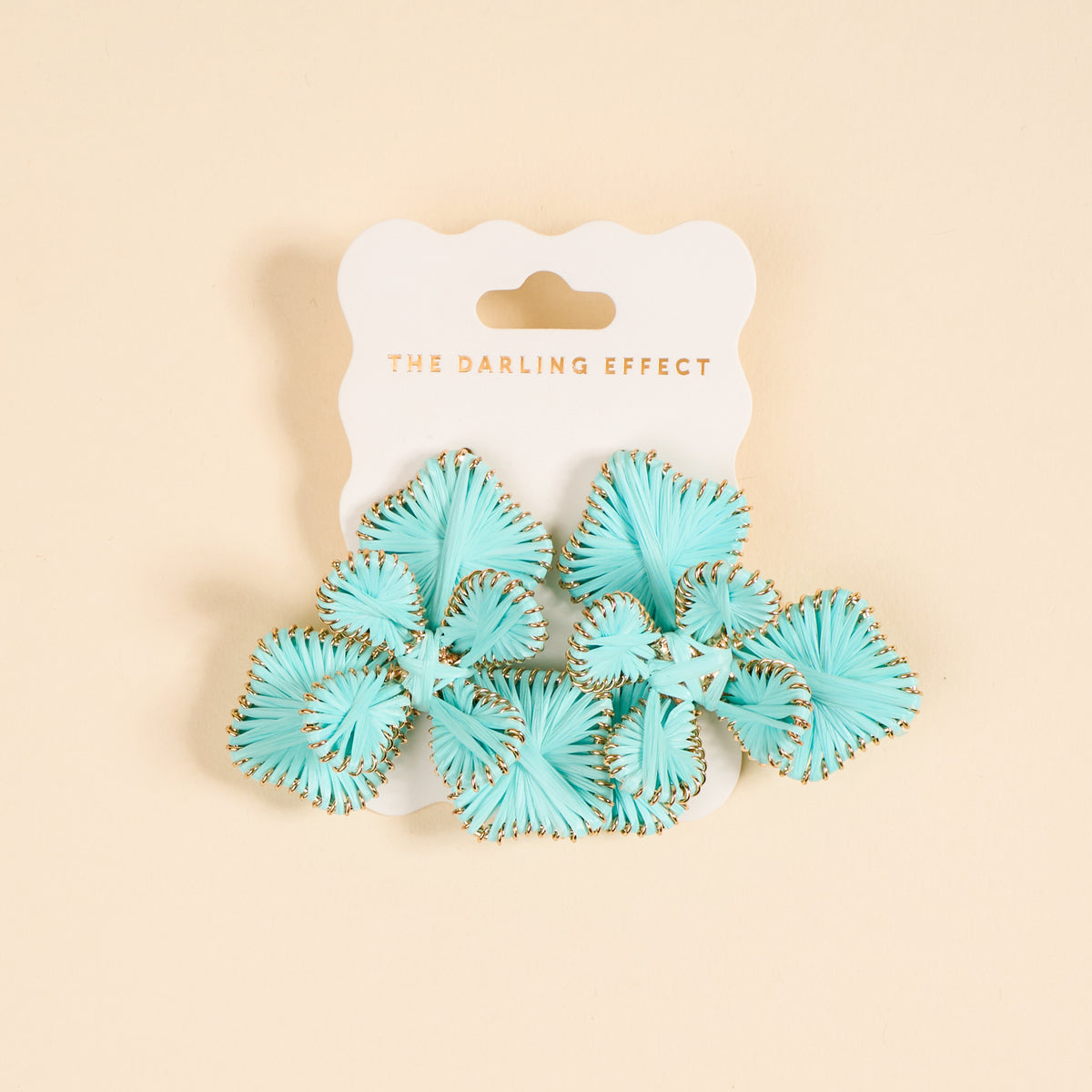 A pair of light blue fan-shaped "Blue Main Character Earrings" by The Darling Effect, with gold edges, perfect for everyday wear, displayed on a white card labeled THE DARLING EFFECT in gold text and set against a beige background.