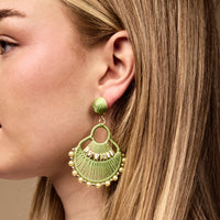 A close-up of a woman’s ear wearing The Darling Effect's Green Paloma Drop Earrings—bold, lime green, fan-shaped accessories with gold accents and pearl-like beads that add an eye-catching yet lightweight touch to any outfit.