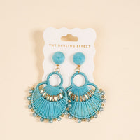 The Darling Effect's Teal Paloma Drop Earrings feature teal thread fans with gold and pearl accents, hanging from a white card. Lightweight and stylish, they're perfect for everyday wear.