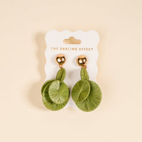 Green Pretty and Polished Earrings by The Darling Effect feature round green leaf-patterned designs with gold studs—ideal for elevating your everyday style. Shown on a white card against a beige background.