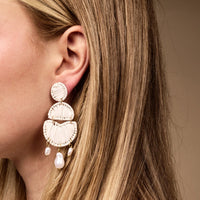 Close-up of a woman's ear with long blonde hair, wearing The Darling Effect's White Pearl Affair Earrings—large white boho earrings with three semicircular segments and dangling pearl-like beads; lightweight for everyday wear.
