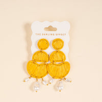 The Darling Effect's Yellow Pearl Affair Earrings feature bright yellow boho woven designs with three stacked shapes and dangling white faux pearls, perfect for everyday wear, shown on a branded card against a light beige background.