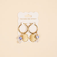 The Darling Effect's Shell Belle Signature Hoop Earrings feature gold hoops with shell charms, blue and white beads, and pearl accents—stylish charm earrings to elevate any look.