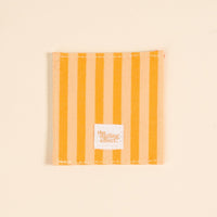 A square fabric coaster with vertical yellow and light beige stripes, white stitching, and a small "The Darling Effect" label. Perfect paired with the Italian Summer Corner Keeper Fabric Bookmark or as a thoughtful gift for book lovers.