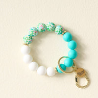 The Darling Effect Cabana Crush Hands-Free Keychain Wristlet features white, turquoise, and green floral silicone beads with gold accents and a keyring charm—combining style and convenience in one chic accessory.