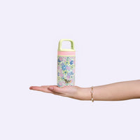 The Darling Effect's Coastal Cove 6 oz Lil' Bitty Bottle, in light green with a floral and sea turtle design, rests on an open palm. Its pink textured band and handle make it the perfect portable hydration companion.