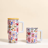 Two white mugs with playful fruit and flower designs sit side by side. The taller one is The Darling Effect's Ciao Bella 20 oz Lifestyle Flip Straw Tumbler with a yellow lid; the shorter mug is open on a beige background.