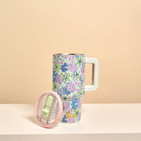 The Darling Effect Coastal Cove 20 oz Lifestyle Flip Straw Tumbler, featuring a pastel floral design and large handle, sits on a white surface with its matching pink-rim lid beside it against a soft beige background.