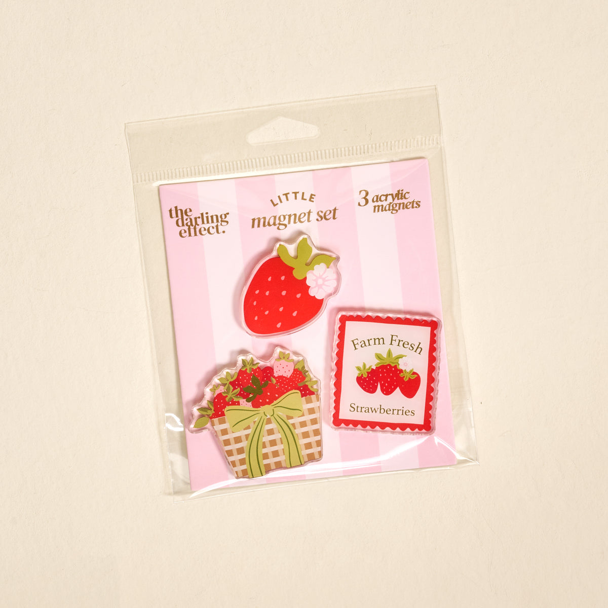 Introducing the Farm Fresh Strawberries Little Magnet Set by The Darling Effect—this delightful package contains three strawberry-themed acrylic magnets: a strawberry, a basket of strawberries, and a “Farm Fresh Strawberries” sign, all arranged on a pink-striped backing. These charming magnets are perfect for brightening up your fridge or adding decorative flair to any kitchen or workspace.