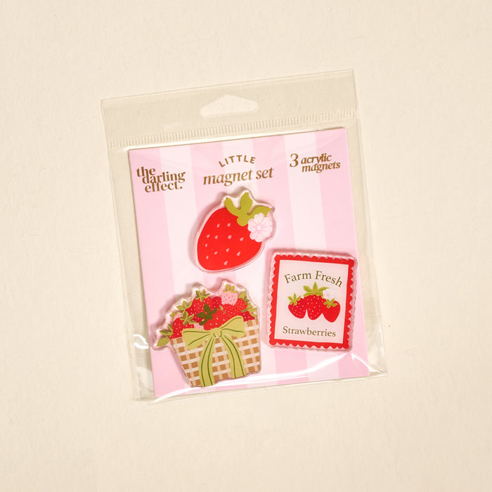 Introducing the Farm Fresh Strawberries Little Magnet Set by The Darling Effect—this delightful package contains three strawberry-themed acrylic magnets: a strawberry, a basket of strawberries, and a “Farm Fresh Strawberries” sign, all arranged on a pink-striped backing. These charming magnets are perfect for brightening up your fridge or adding decorative flair to any kitchen or workspace.
