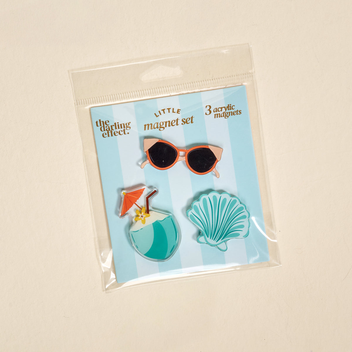 The Darling Effect Vacation Vibes Little Magnet Set features three acrylic fridge magnets—a pair of sunglasses, a blue drink with a straw and umbrella, and a blue seashell—beautifully packaged on a blue and white card labeled “Little magnet set.” These fun magnets make perfect decorative accents for your kitchen or office.