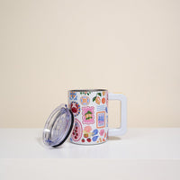 The Darling Effect’s Ciao Bella 14 oz Insulated Mug, featuring colorful floral and patterned designs, sits on a white surface. It has a clear lid and is set against a plain beige background.