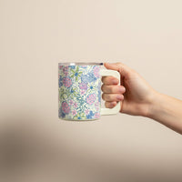 A hand holds The Darling Effect’s Coastal Cove 14 oz Insulated Mug, featuring a pastel pink, blue, and green floral design with double-wall insulation, set against a plain beige background.