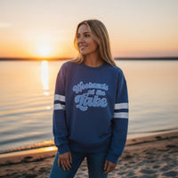 A woman in The Darling Effect’s Weekends at the Lake Oversized Crew smiles on a sandy lakeshore at sunset. The calm water and colorful sky highlight the cozy, relaxed vibe of this comfy sweatshirt.