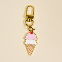 The Darling Effect’s Ice Cream Cone Pawfect Collar Charm features a gold keychain with a pink and white enamel ice cream cone and cherry, perfect for adding a sweet, playful touch to your pet’s accessories or collar charm collection.
