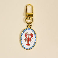 The Darling Effect’s Lobster Pawfect Collar Charm features a gold keychain with an oval enamel lobster design framed by a blue mosaic border—ideal for pet jewelry or adding flair to your pet accessories collection.