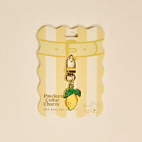 The Lemon Pawfect Collar Charm by The Darling Effect is a gold and yellow lemon-shaped accessory with green leaves. Attached to striped "Pawfect Collar Charm" packaging, it adds playful style to any pet collar and stands out among must-have accessories.